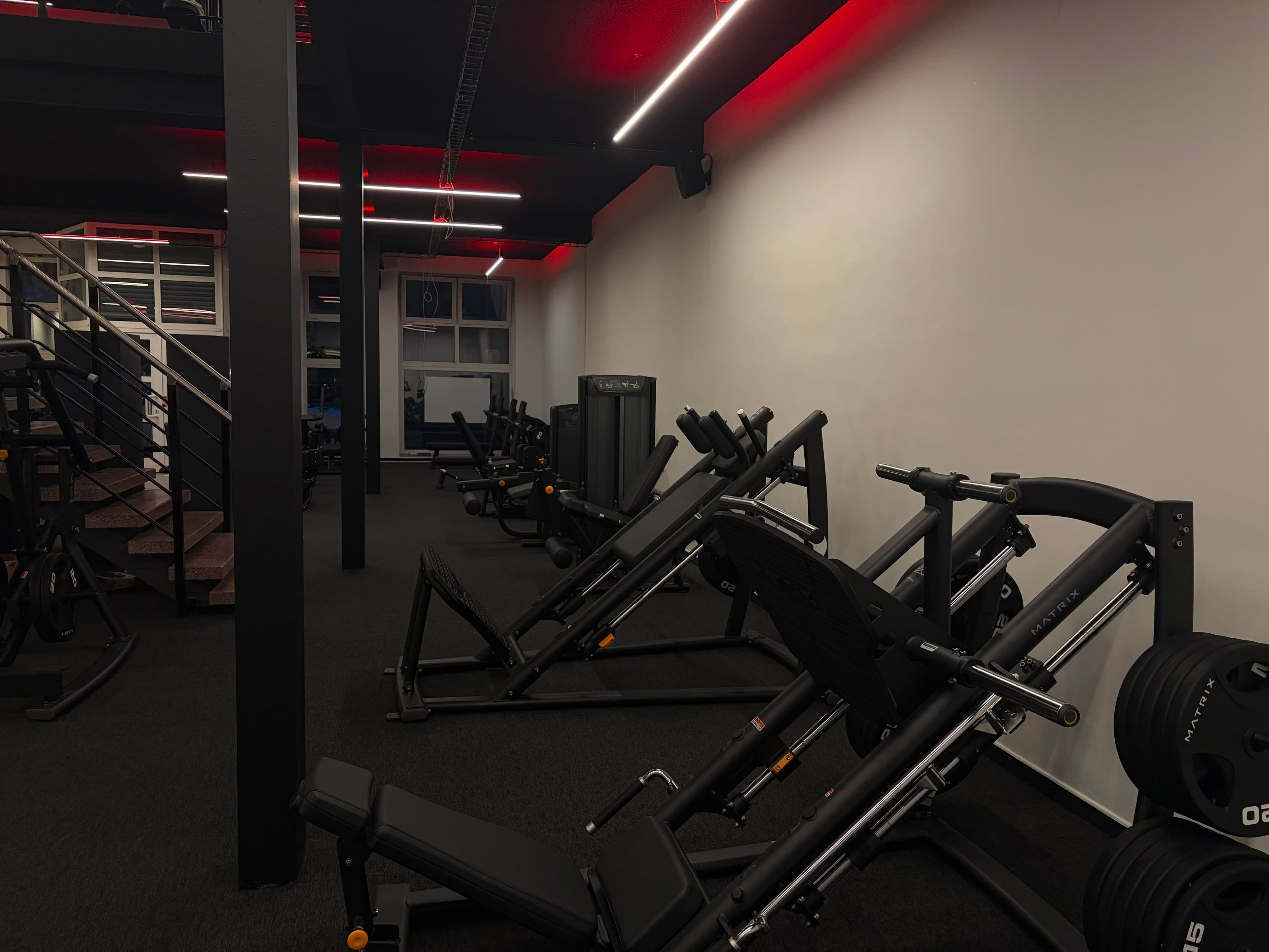 Posilovna NEXT LEVEL GYM – lavice s činkami a červené neonové osvětlení stropu