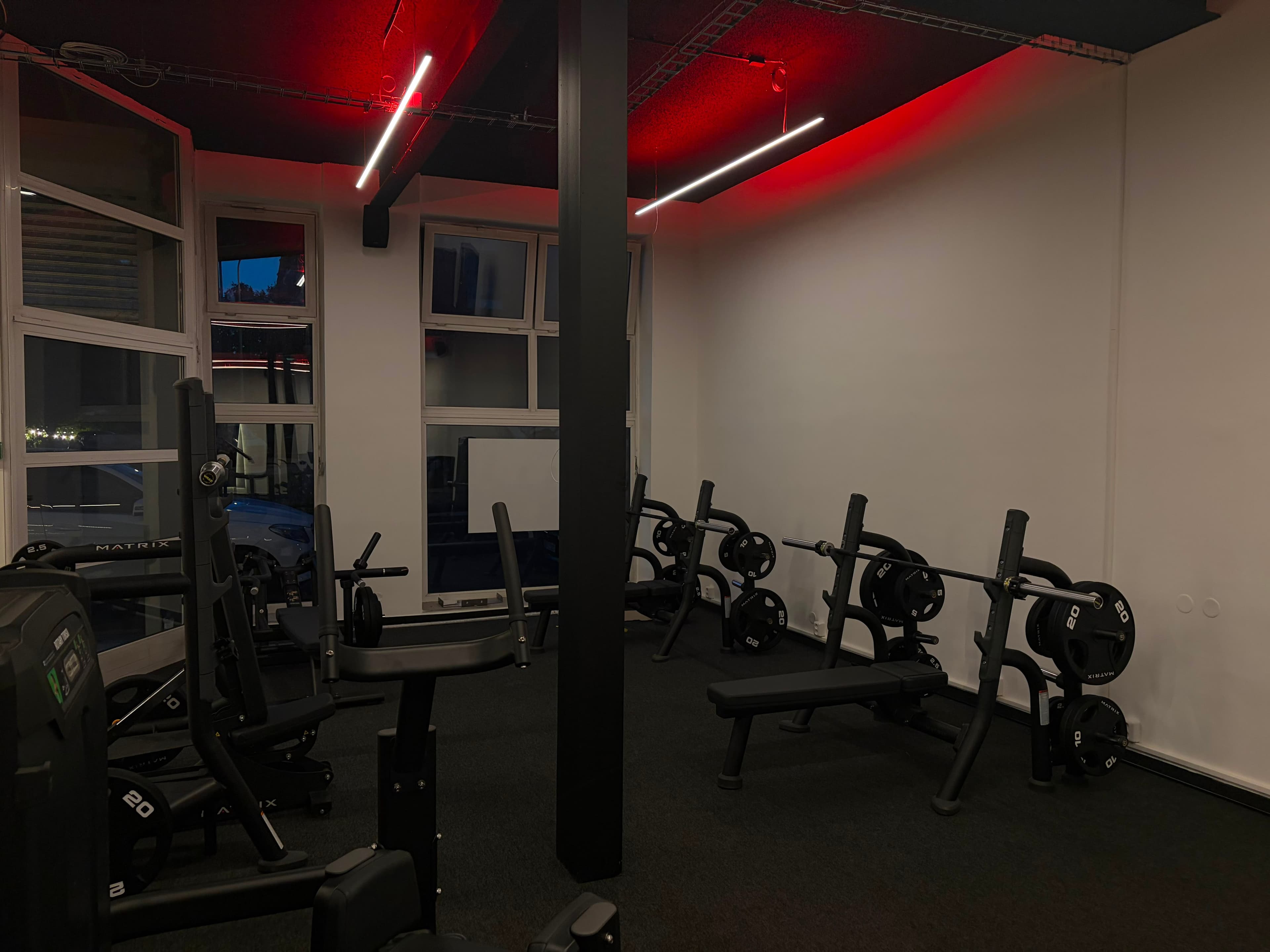Posilovna NEXT LEVEL GYM – posilovací stroje a schodiště, červené podsvícení stropu